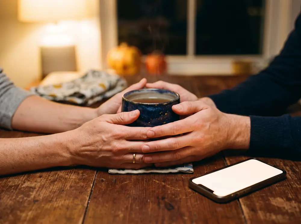 Two people holding one warm mug together at a kitchen table